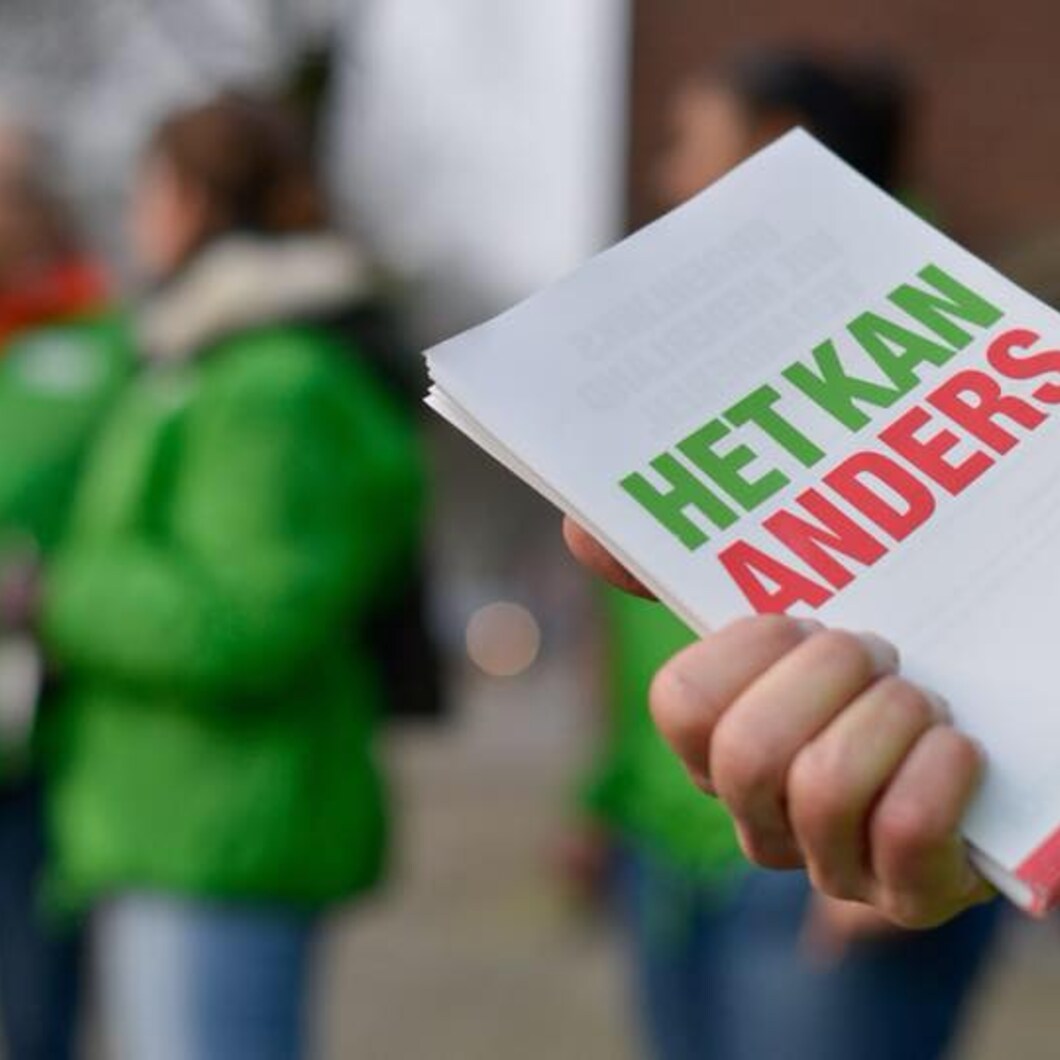 Iemand houdt GroenLinks-flyers vast met daarop: "Het kan anders". De persoon draagt een groen jasje. Op de achtergrond staan meer mensen in groene jasjes.