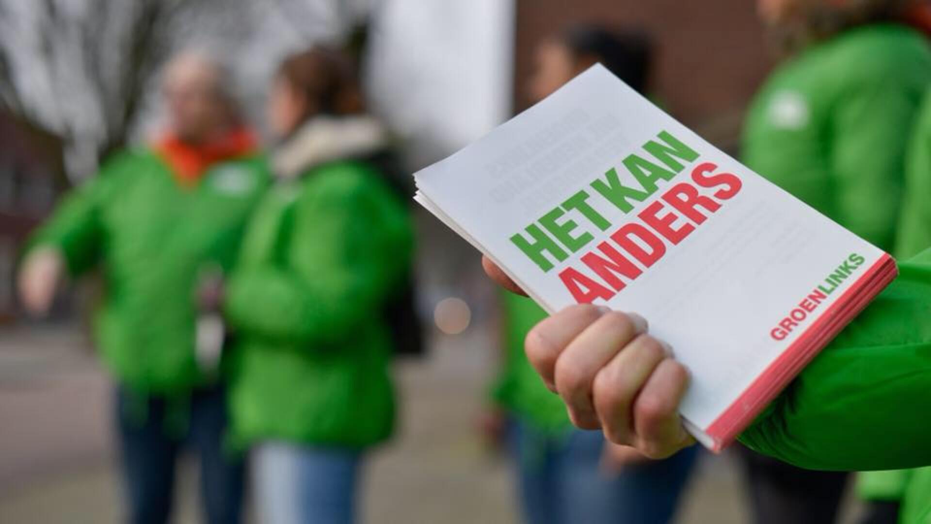 Iemand houdt GroenLinks-flyers vast met daarop: "Het kan anders". De persoon draagt een groen jasje. Op de achtergrond staan meer mensen in groene jasjes.